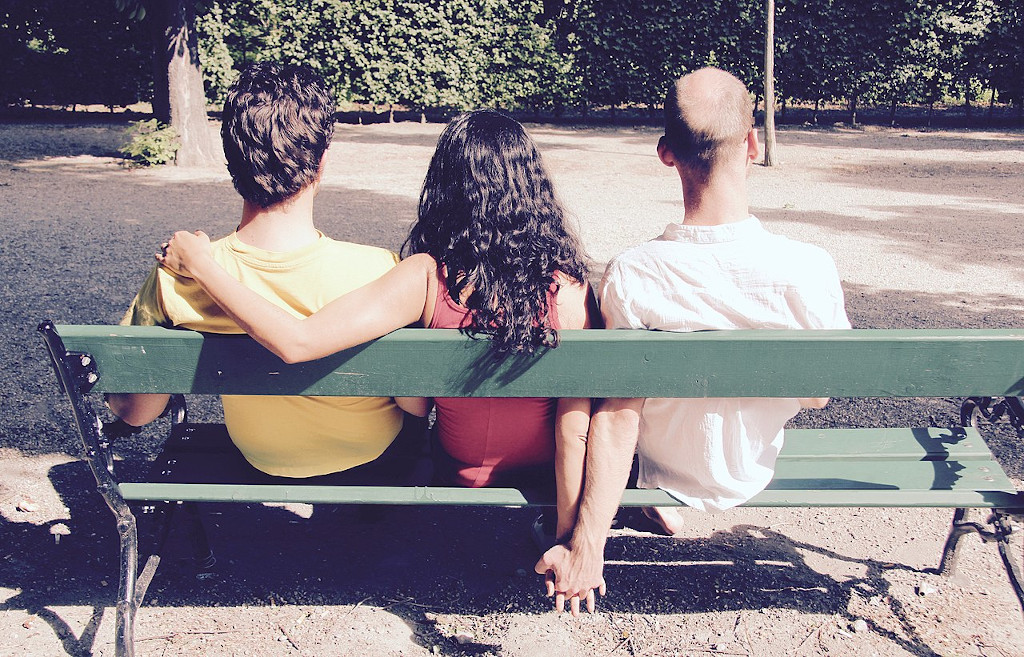 Trois personnes assises sur un banc, l'une ayant le bras autour des épaules de l'autre et tenant la troisième par la main.